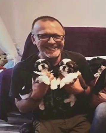 Marcin Wierzba siedzi na kanapie i trzyma dwa szczeniaki.